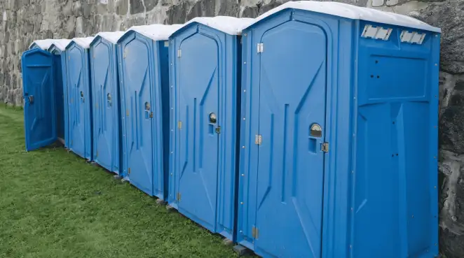 Row of blue portable toilets lined up on grass against a stone wall for event sanitation in Savannah, GA