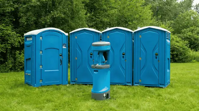Four blue portable toilets and a matching hand washing station on grass near trees, a common sight at local outdoor events in Savannah, GA