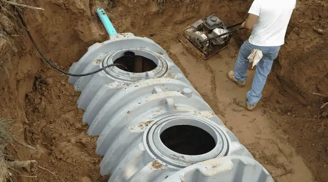 Septic tank installation showing a technician compacting soil around a new poly septic tank in an excavation pit in Savannah, GA